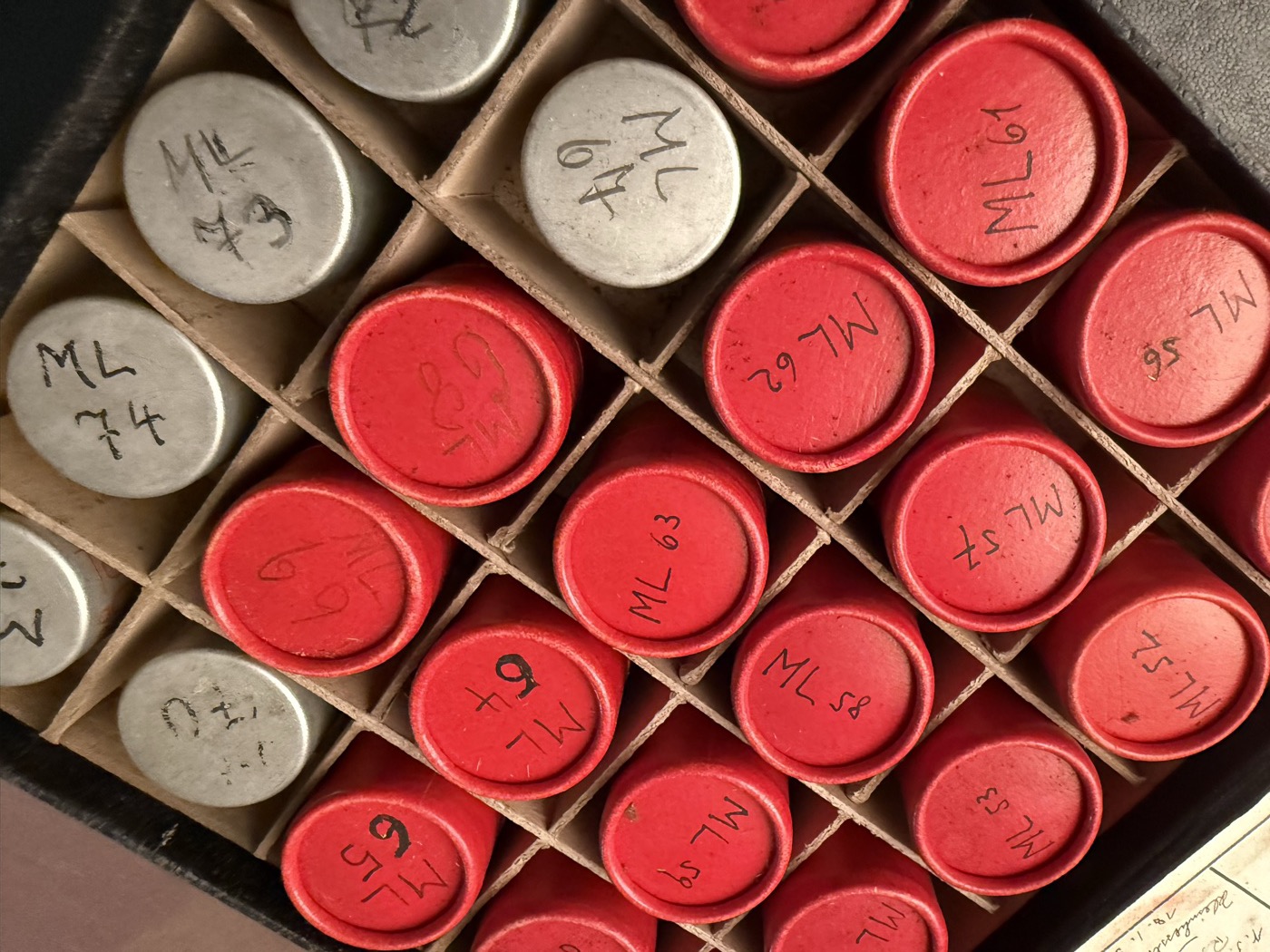 Beschriftete rote und helle Filmdosen in einem Archivkasten